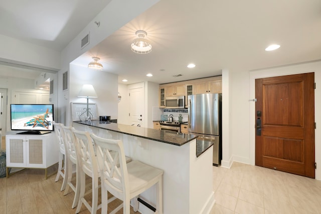 kitchen featuring dark stone countertops, kitchen peninsula, appliances with stainless steel finishes, a kitchen bar, and backsplash