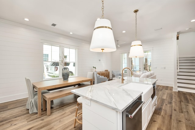 kitchen with white cabinets, an island with sink, pendant lighting, sink, and hardwood / wood-style floors