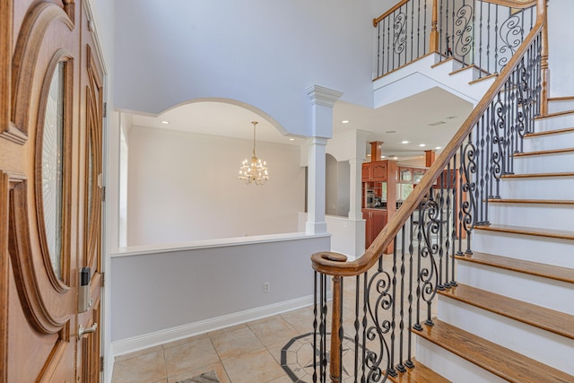 staircase with tile patterned flooring, a high ceiling, decorative columns, and an inviting chandelier