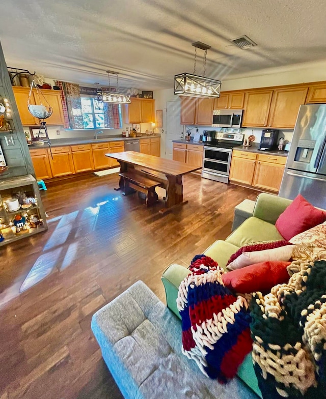 kitchen featuring appliances with stainless steel finishes, hanging light fixtures, dark hardwood / wood-style floors, and a textured ceiling