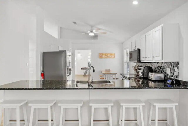 kitchen with white cabinets, sink, stainless steel appliances, a breakfast bar, and dark stone counters