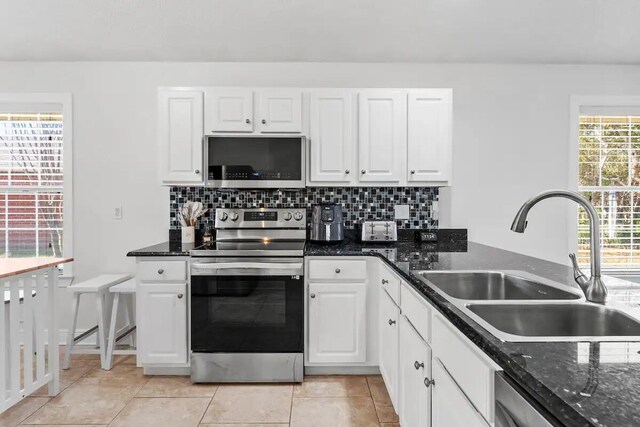 kitchen with tasteful backsplash, dark stone counters, sink, white cabinets, and appliances with stainless steel finishes