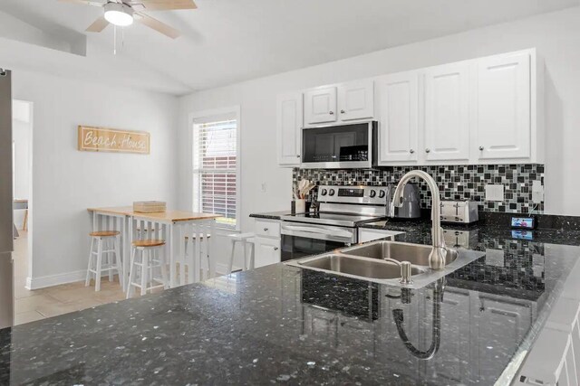 kitchen with white cabinets, sink, stainless steel appliances, dark stone countertops, and decorative backsplash