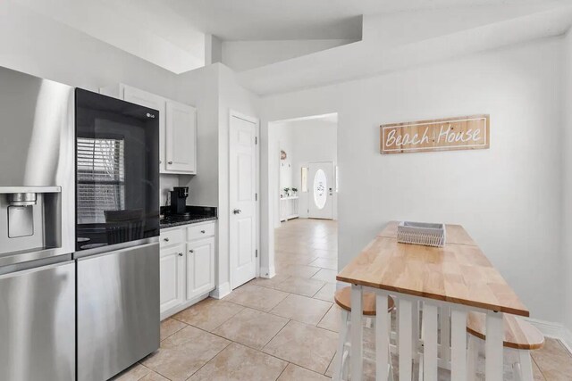 kitchen featuring light tile patterned flooring, lofted ceiling, white cabinetry, and stainless steel refrigerator with ice dispenser