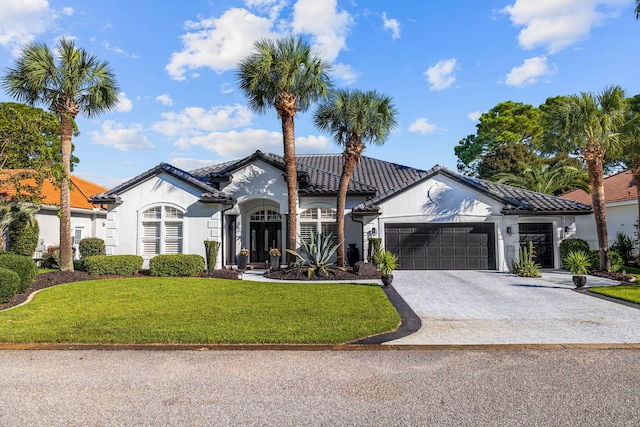 view of front of property with an attached garage, a tile roof, stucco siding, a front yard, and decorative driveway