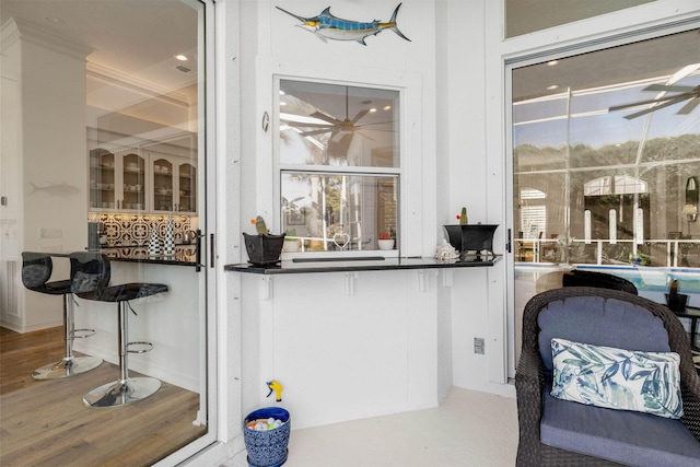 bar featuring ceiling fan, ornamental molding, and wood finished floors