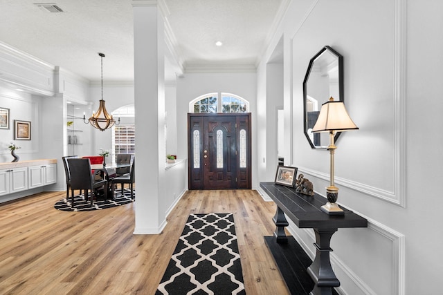 foyer featuring light wood-type flooring, crown molding, a chandelier, and a textured ceiling