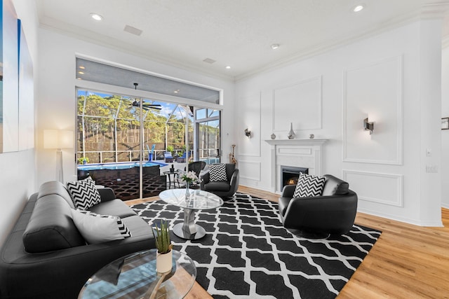 living room featuring ornamental molding, wood finished floors, a decorative wall, a sunroom, and recessed lighting