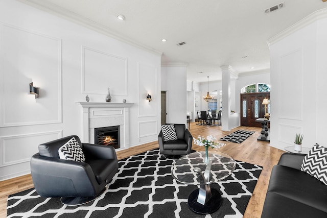 living room with ornamental molding, an inviting chandelier, a fireplace, and light hardwood / wood-style floors