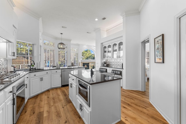 kitchen with a kitchen island, dark countertops, white cabinetry, a sink, and stainless steel appliances
