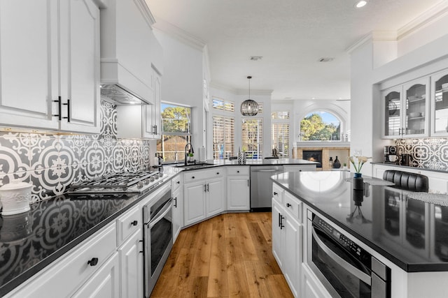 kitchen with stainless steel appliances, custom range hood, white cabinetry, and a healthy amount of sunlight