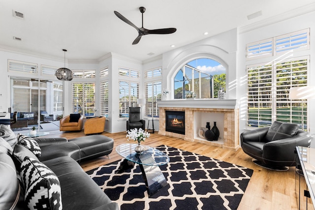 living area with crown molding, ceiling fan, a glass covered fireplace, wood finished floors, and visible vents