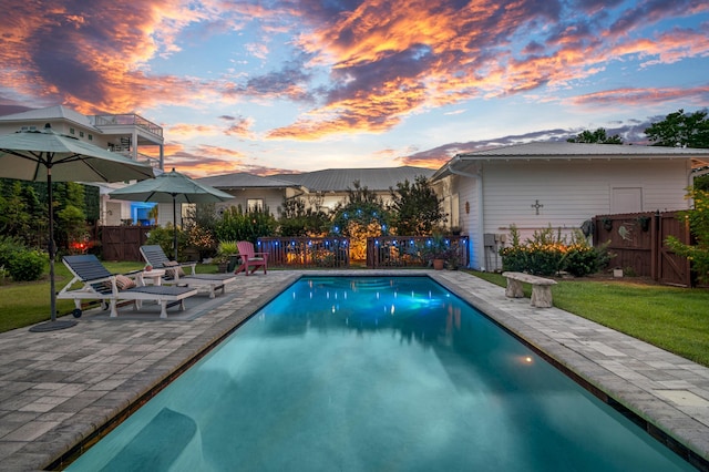 pool at dusk with a lawn and a patio area