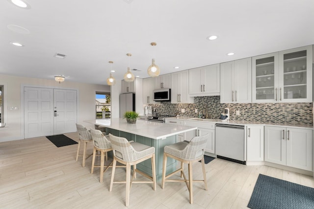 kitchen featuring stainless steel appliances, hanging light fixtures, white cabinetry, a breakfast bar area, and light hardwood / wood-style flooring