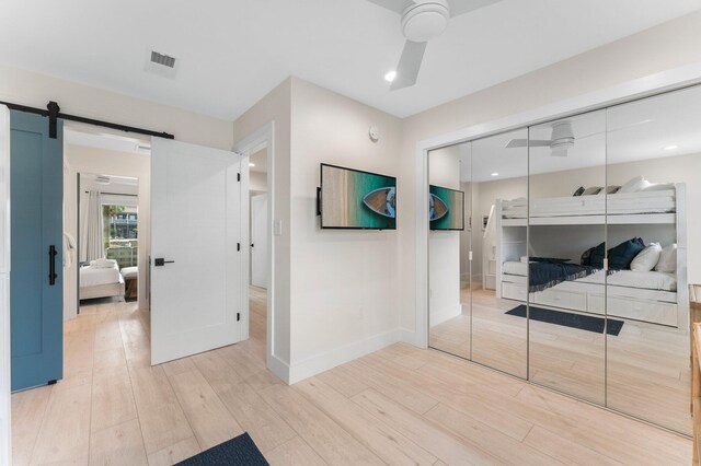 bedroom featuring ceiling fan, a barn door, a closet, and wood-type flooring