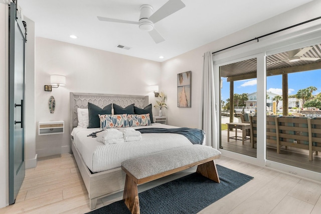 bedroom featuring access to outside, ceiling fan, light hardwood / wood-style flooring, a barn door, and an AC wall unit