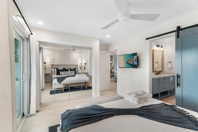 bedroom with a barn door, light hardwood / wood-style floors, ceiling fan, a closet, and ensuite bath