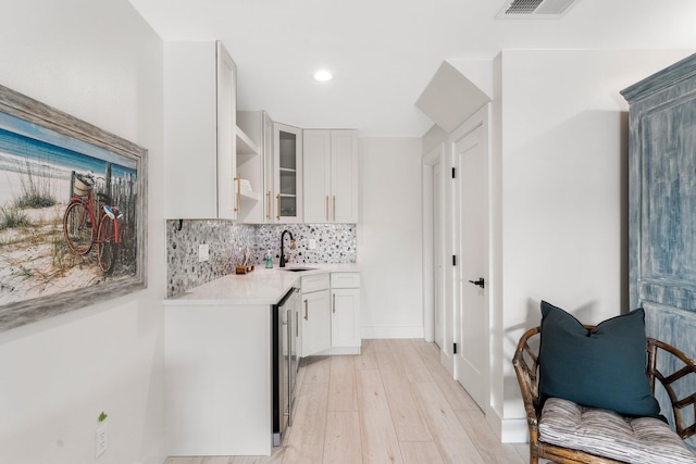 kitchen featuring tasteful backsplash, sink, light wood-type flooring, and white cabinetry