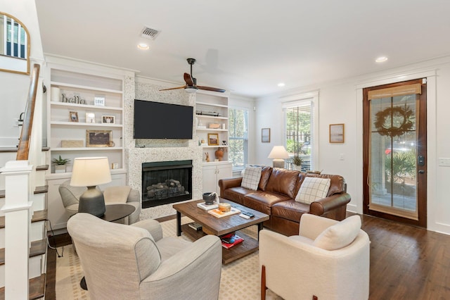 living room featuring wood-type flooring, a fireplace, ceiling fan, ornamental molding, and built in shelves