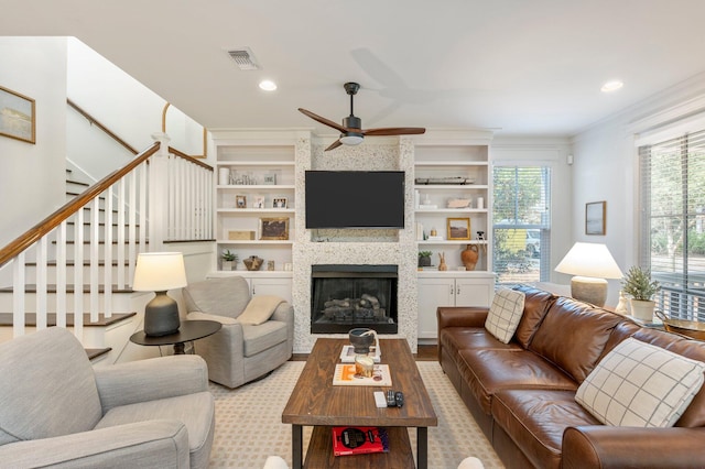 living room with ornamental molding, ceiling fan, a fireplace, and built in shelves