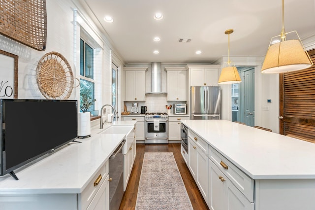 kitchen with hanging light fixtures, white cabinetry, a large island, stainless steel appliances, and wall chimney exhaust hood