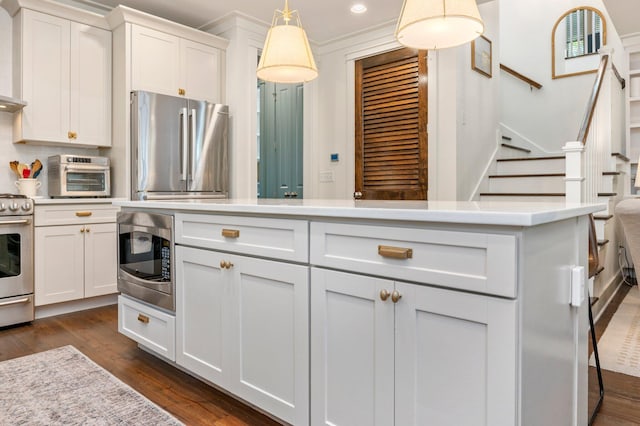 kitchen with dark wood-type flooring, ornamental molding, white cabinets, pendant lighting, and appliances with stainless steel finishes