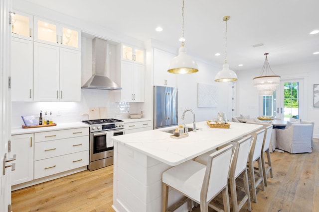 kitchen featuring wall chimney exhaust hood, light hardwood / wood-style floors, a kitchen island with sink, appliances with stainless steel finishes, and white cabinetry