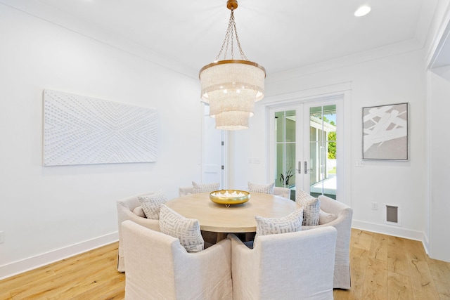 dining area featuring light wood-type flooring, a notable chandelier, crown molding, and french doors