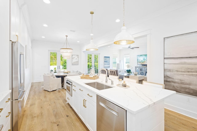 kitchen featuring white cabinets, an island with sink, hanging light fixtures, sink, and appliances with stainless steel finishes