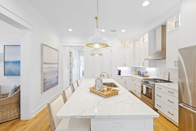 kitchen featuring an island with sink, stainless steel appliances, wall chimney exhaust hood, and sink