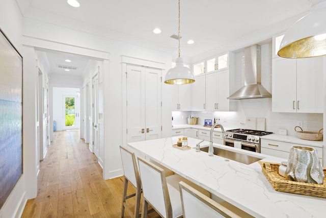 kitchen featuring light wood-type flooring, light stone countertops, white cabinets, wall chimney exhaust hood, and high end stove