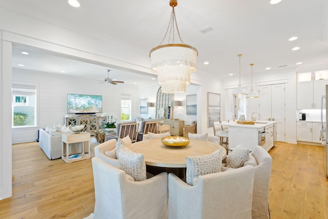 dining room featuring ceiling fan with notable chandelier, light wood-type flooring, and sink