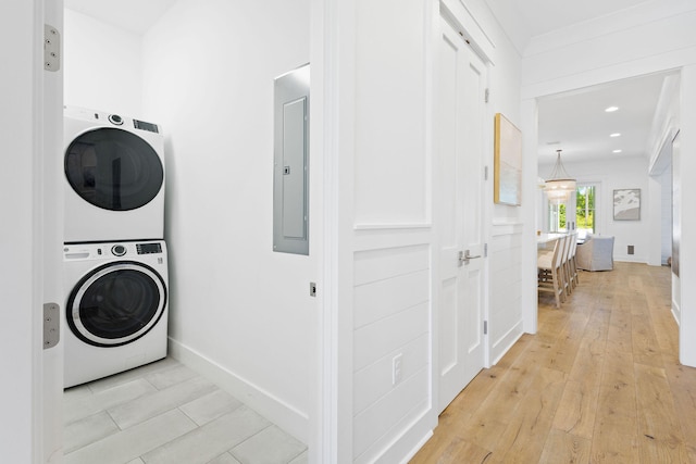 laundry room featuring electric panel, stacked washer and dryer, and light wood-type flooring