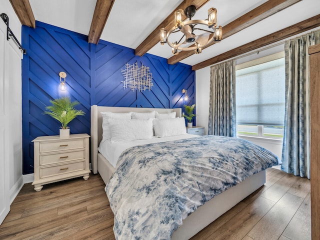 bedroom featuring beam ceiling, dark wood-type flooring, a barn door, and a notable chandelier