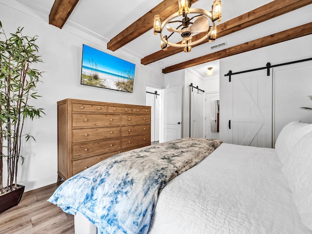 bedroom featuring beam ceiling, hardwood / wood-style floors, a barn door, and a notable chandelier