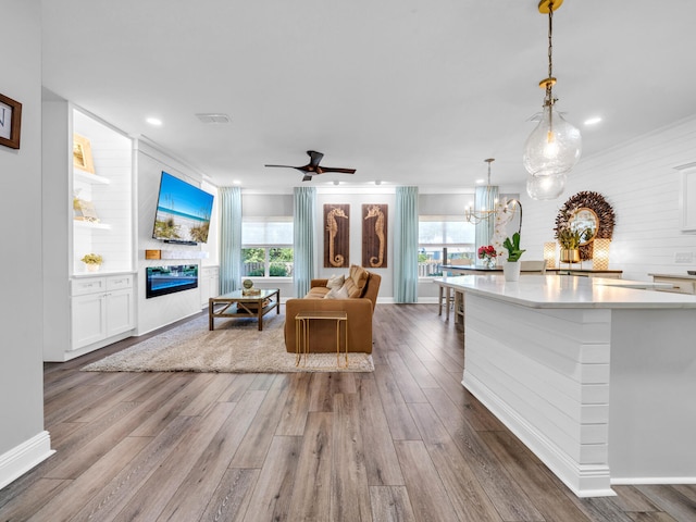 living room with hardwood / wood-style floors, crown molding, and ceiling fan with notable chandelier