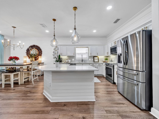 kitchen with a kitchen island, appliances with stainless steel finishes, white cabinetry, and light hardwood / wood-style floors