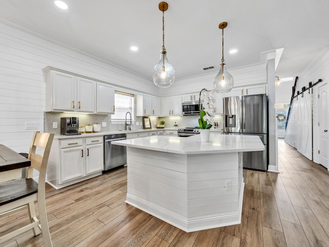 kitchen featuring a kitchen island, a barn door, decorative light fixtures, white cabinetry, and appliances with stainless steel finishes