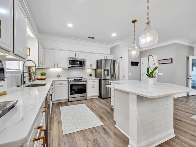 kitchen featuring white cabinets, hanging light fixtures, a kitchen island, appliances with stainless steel finishes, and sink