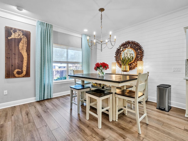 dining area with light hardwood / wood-style floors, an inviting chandelier, wooden walls, and crown molding