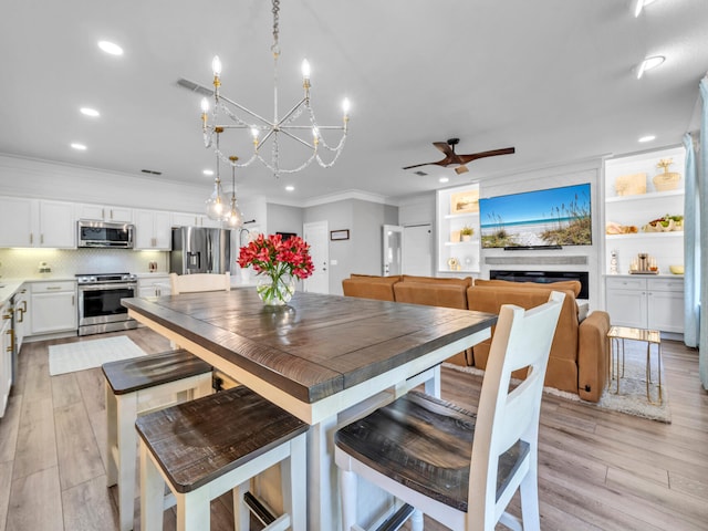 dining room featuring built in shelves, crown molding, ceiling fan with notable chandelier, and light hardwood / wood-style floors