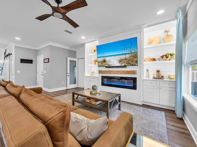 living room featuring crown molding, dark hardwood / wood-style floors, a large fireplace, and ceiling fan