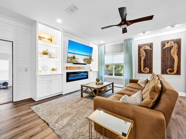 living room with ceiling fan, hardwood / wood-style flooring, wooden walls, and a fireplace