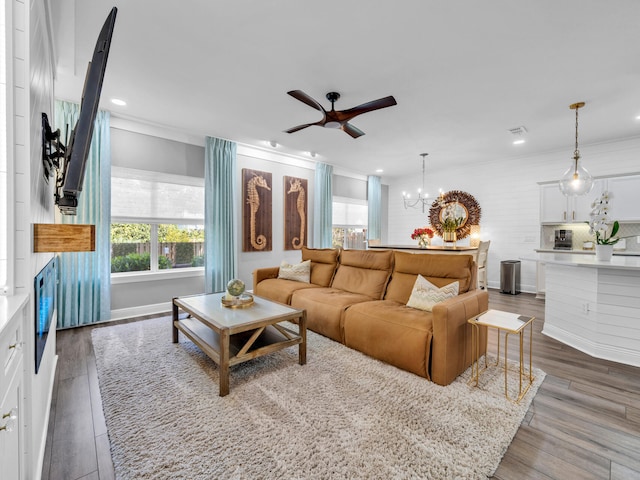 living room with hardwood / wood-style flooring, ornamental molding, and ceiling fan with notable chandelier