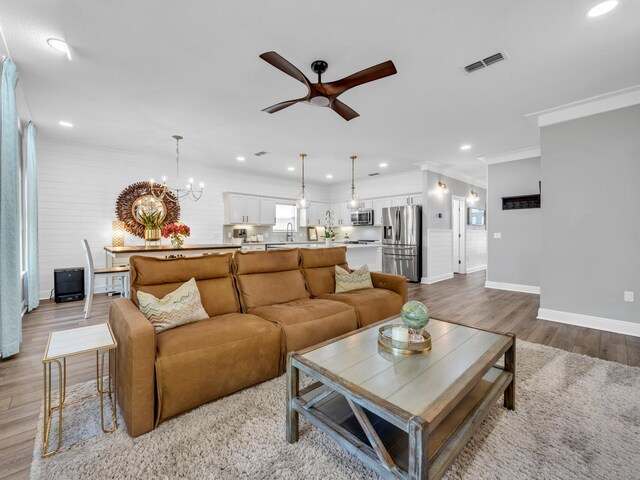 living room with light hardwood / wood-style flooring, ornamental molding, sink, and ceiling fan with notable chandelier