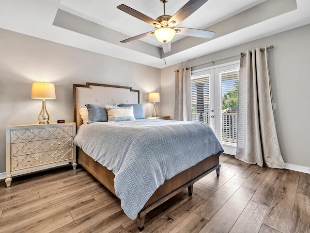 bedroom with ceiling fan, wood-type flooring, and a raised ceiling