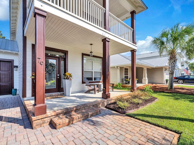 view of exterior entry with a porch, a balcony, and a lawn