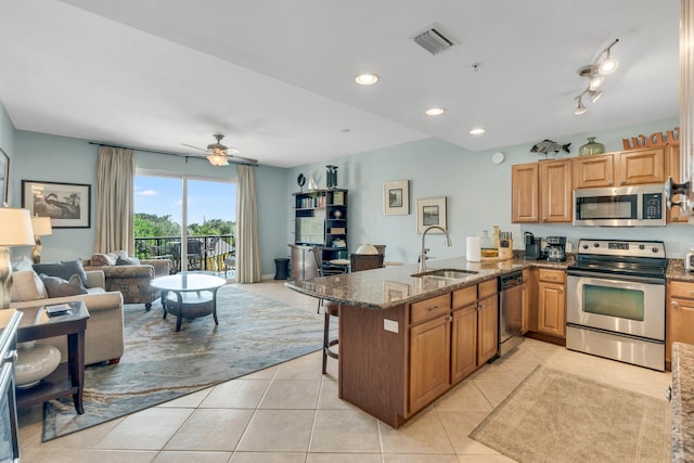 kitchen with sink, kitchen peninsula, appliances with stainless steel finishes, a breakfast bar area, and dark stone counters