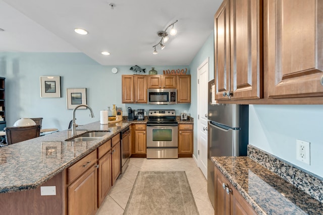 kitchen with light tile patterned floors, sink, a kitchen island with sink, appliances with stainless steel finishes, and dark stone countertops