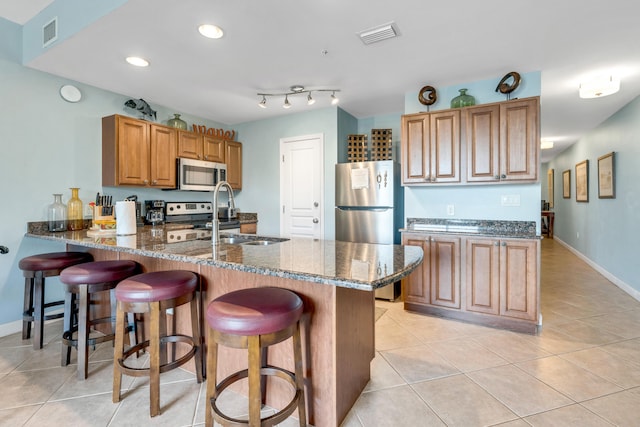 kitchen featuring dark stone countertops, appliances with stainless steel finishes, kitchen peninsula, and a kitchen breakfast bar